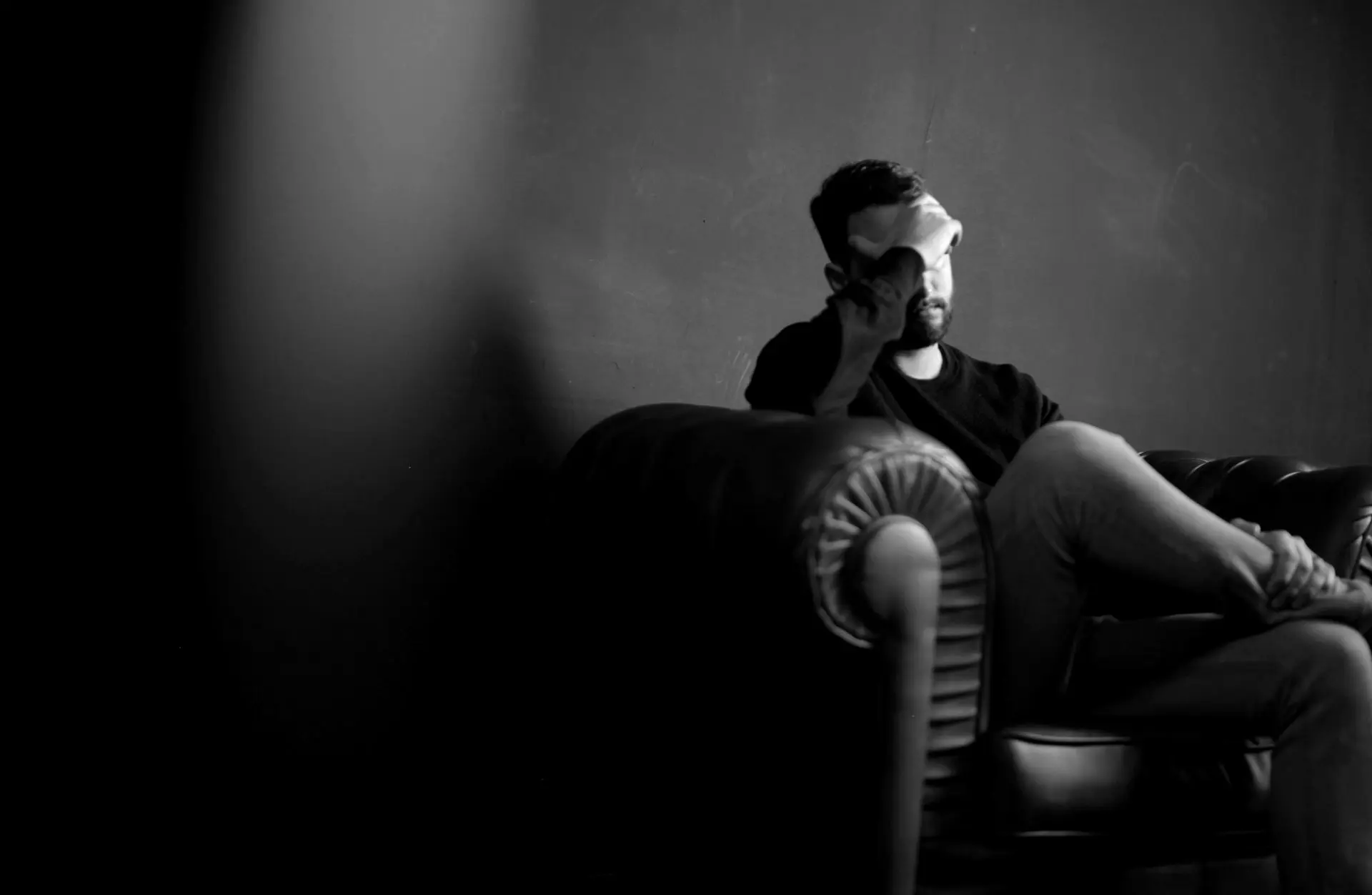 a man holds his head while sitting on a sofa