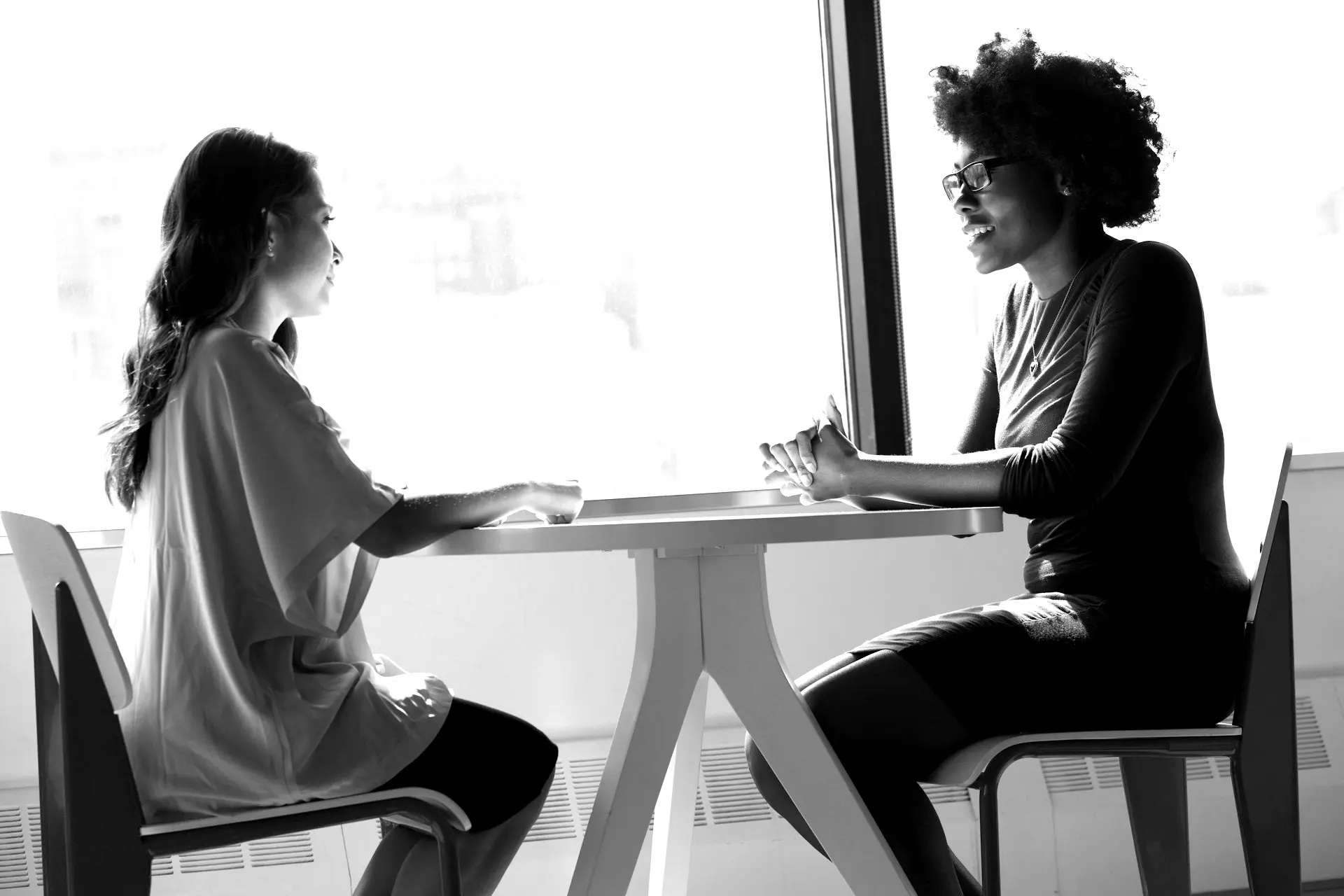 two women sitting beside table and talking