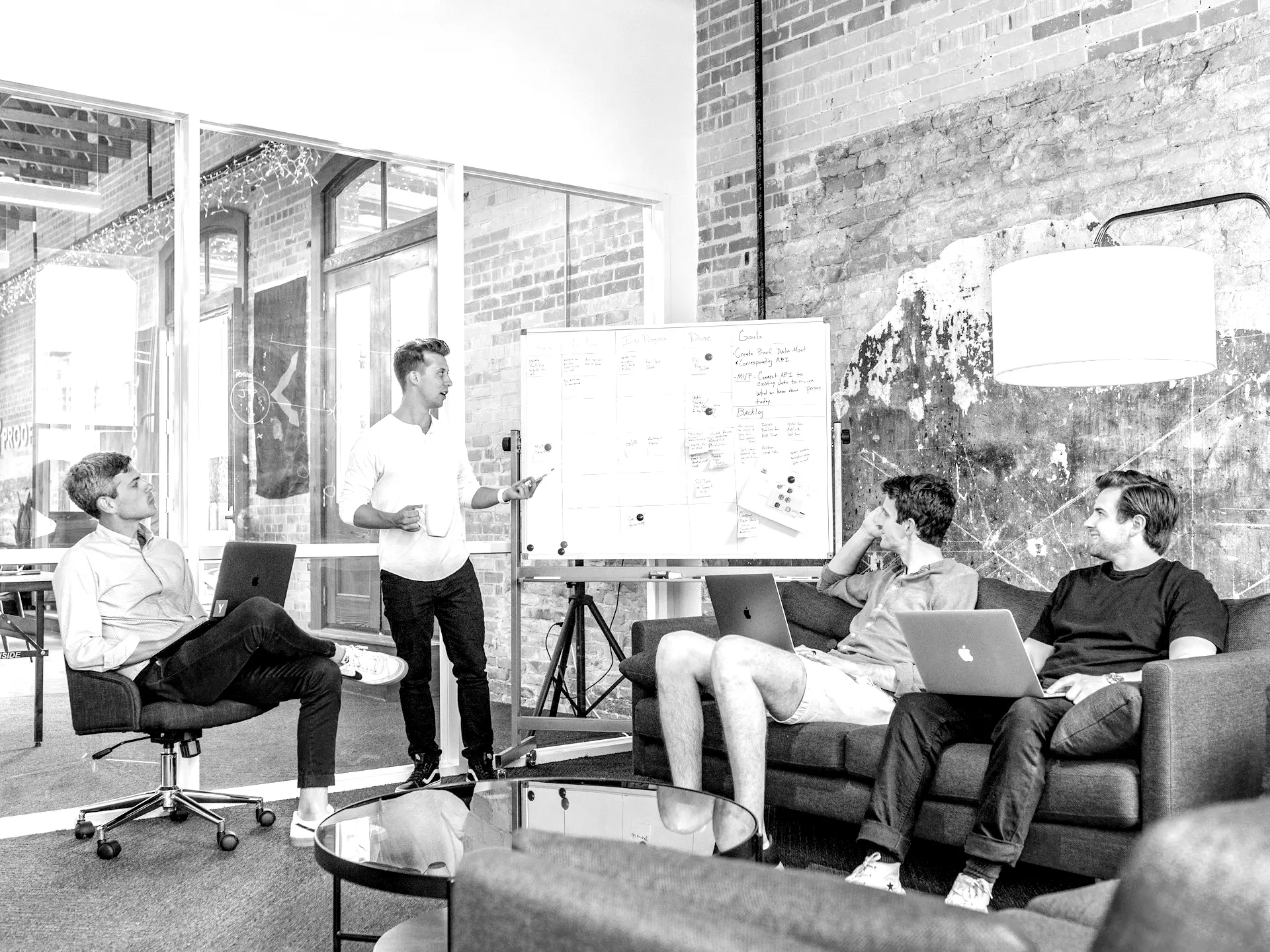 three men sitting while using laptops and watching man beside whiteboard